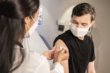 A man looks at his upper arm where a woman places a bandaid. 