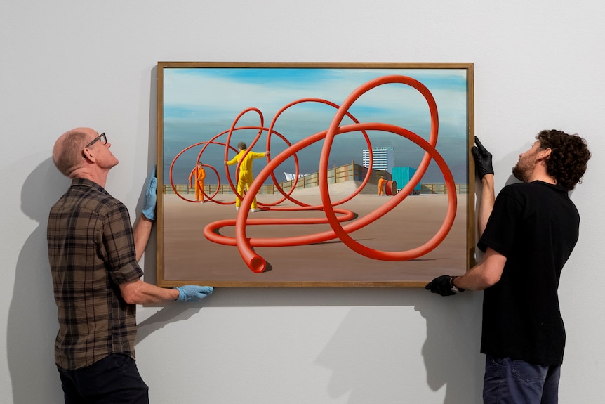 Two men hang a Jeffrey Smart paining of intertwining poles.