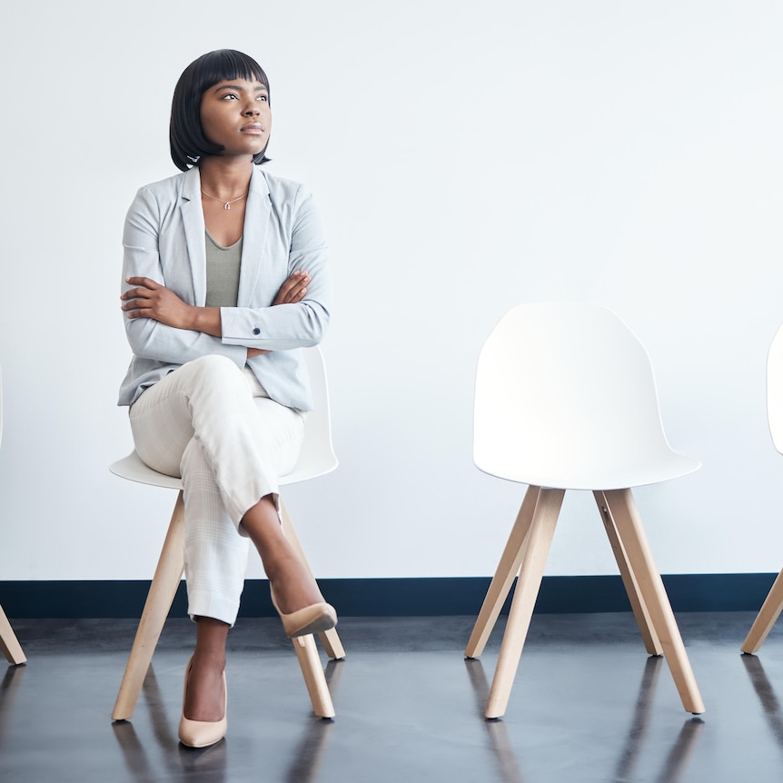 A young businesswoman sits alone in a row of four white chairs