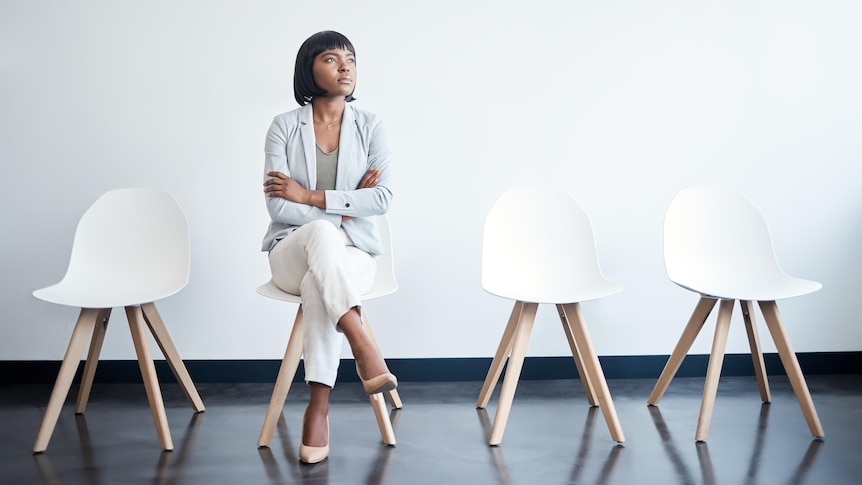 A young businesswoman sits alone in a row of four white chairs