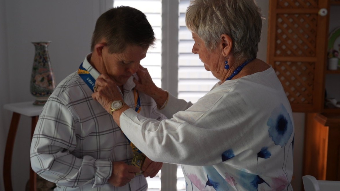 A woman places a medal around her adult son's neck.