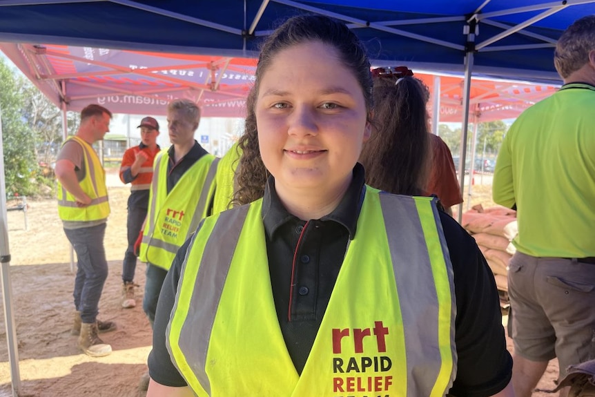 A smiling young woman wearing a high-vis vest.