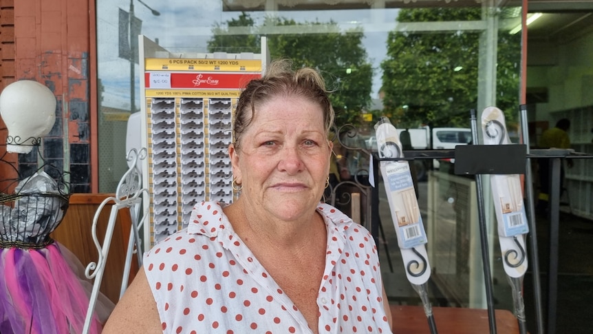 A woman in a sleeveless top stands outside her flooded business.