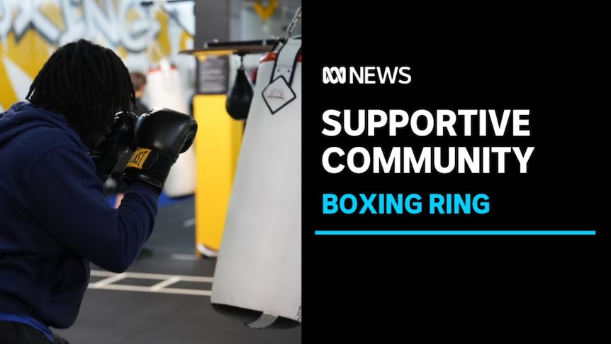 Supportive Community, Boxing Ring: A man wearing boxing gloves holds up his fists in front of a sparring bag.