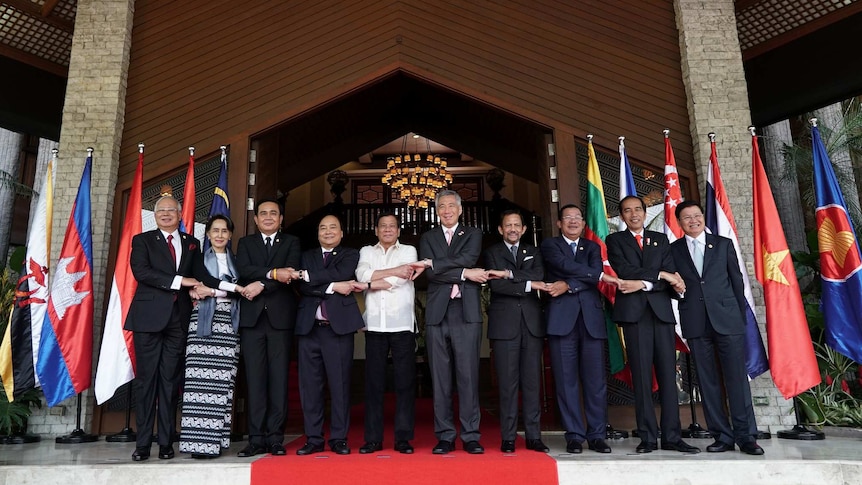 10 ASEAN leaders, standing in front of the flags of their countries, link hands