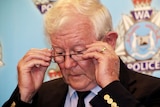 A close-up photo of Denis Glennon adjusting his reading glasses in front of a police backdrop.