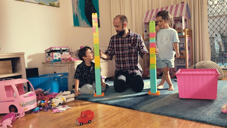 Two children with building blocks and their father between them