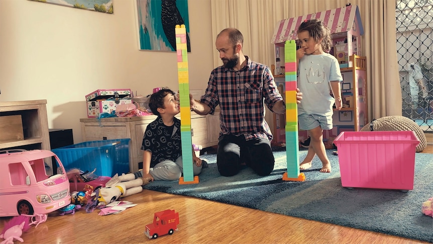 Two children with building blocks and their father between them