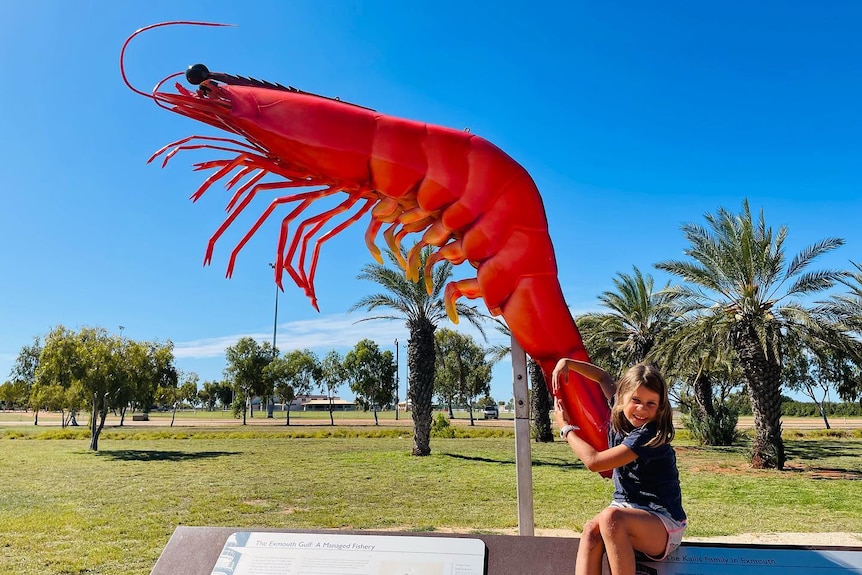 Girl pretends to hug giant prawn statue. 
