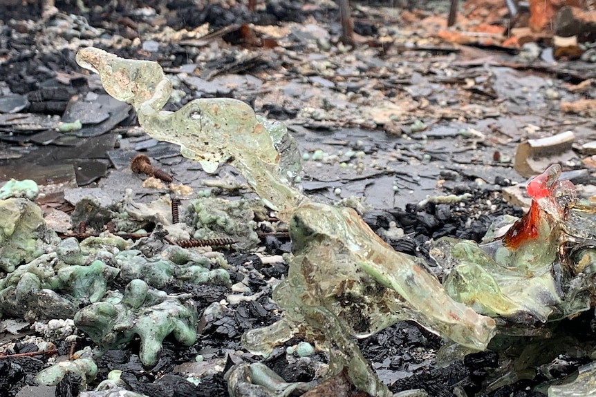 Mangled light green glass pointing upwards sits on black debris.