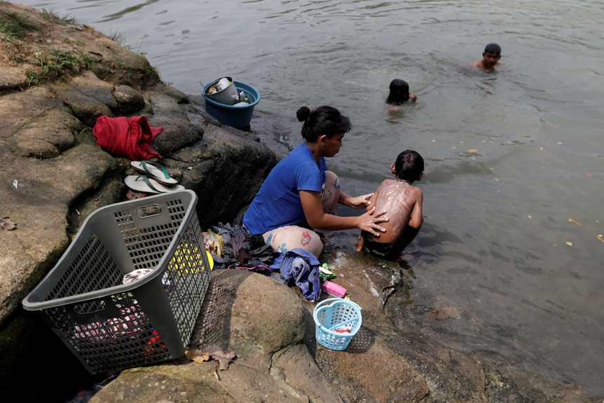 A woman bathes her young son while washing clothes in the Cisadane River