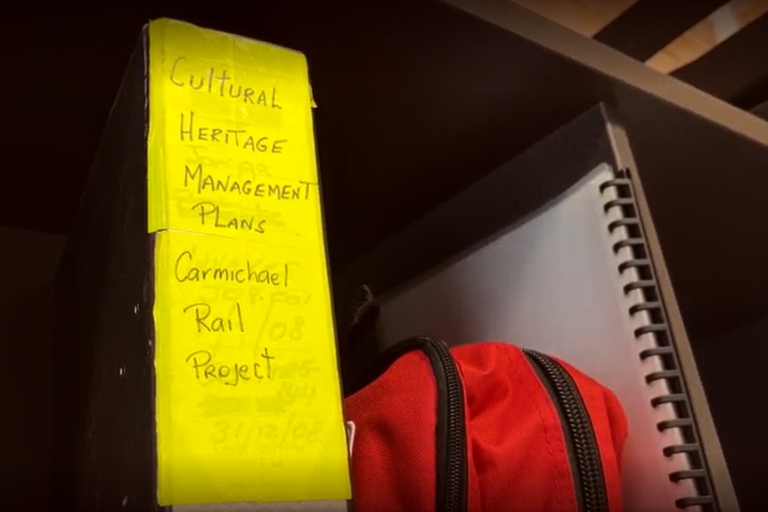 a bright yellow handwritten label on a binder, which says "cultural heritage management plans, Carmichael Rail project"