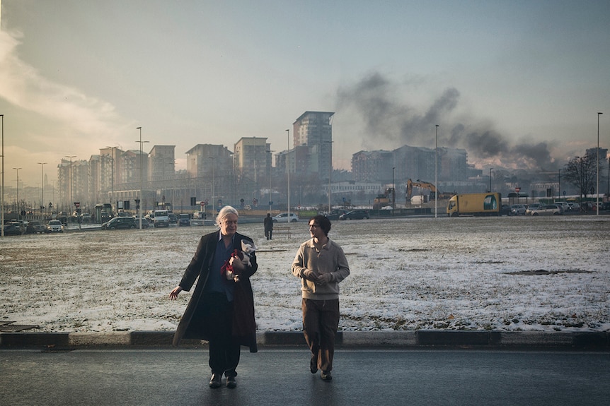 Colour still of Tommaso Ragno and Adriano Tardiolo walking away from an industrial cityscape in 2018 film Happy as Lazzaro.