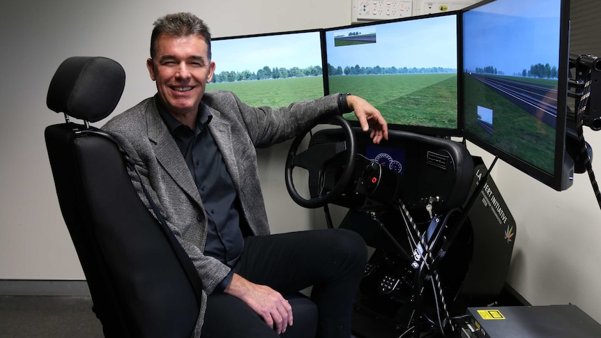 Professor Iain McGregor turns towards the camera from the seat of a driver simulation chair.