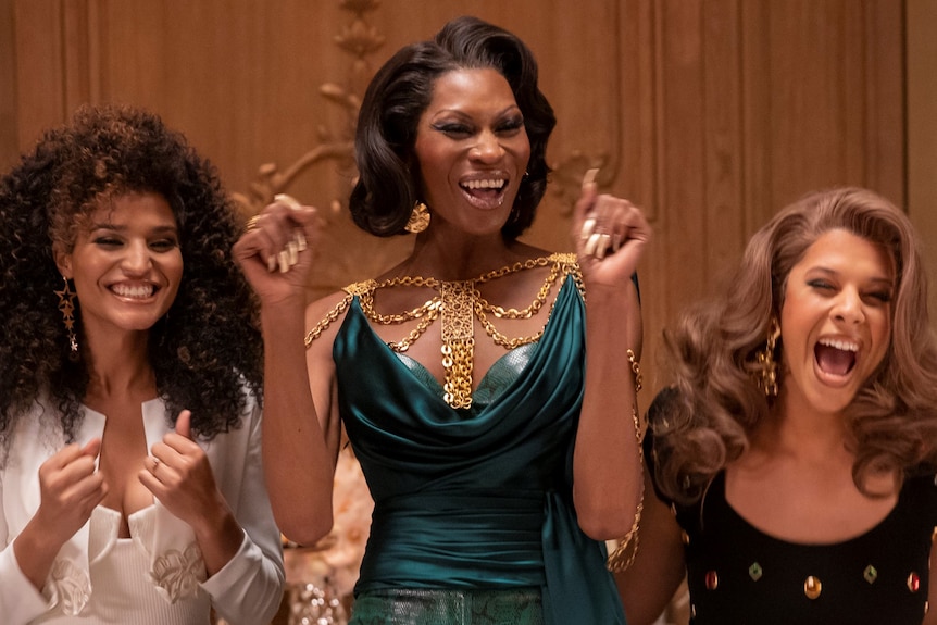 Four happy trans black and latinx women stand in a row in fancy outfits at a wedding reception in the tv show Pose