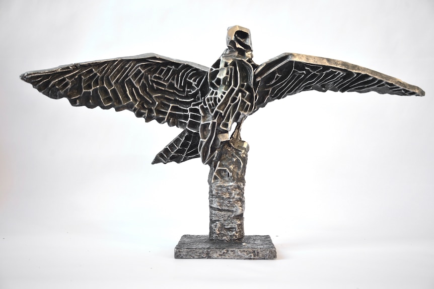 bronze statue of eagle with wings spread out perched on a tree branch. The body and underwing textured like a maze.