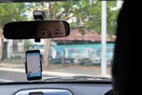 A photo from inside a car that shows the reflection of Yogesh Thapaliya as well as the Hi Oscar app.