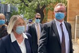 A woman and man wearing suits and face masks on a city street 