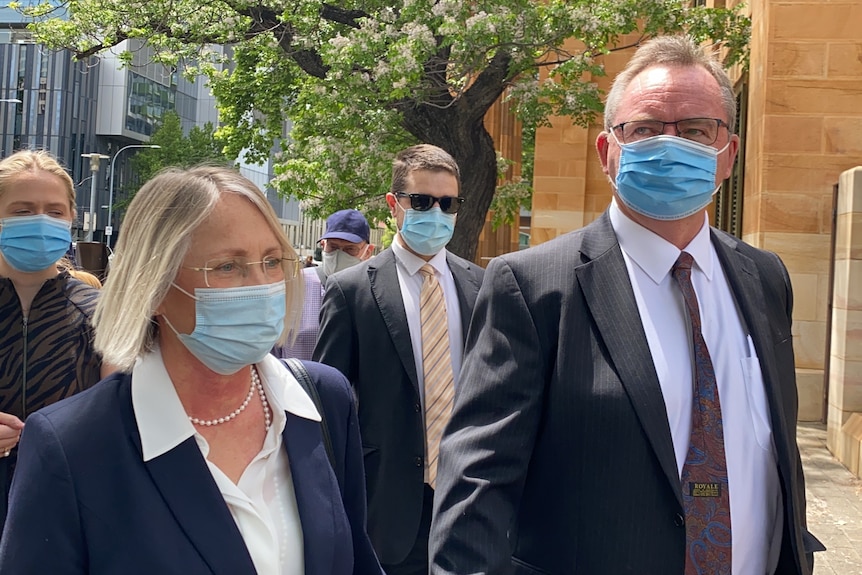 A woman and man wearing suits and face masks on a city street 