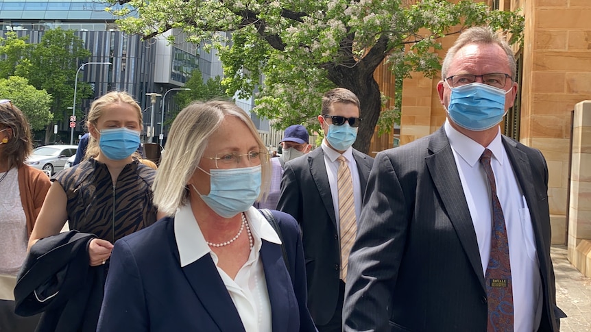 A woman and man wearing suits and face masks on a city street 