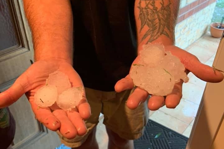 Trois grêlons de la taille d'une balle de golf remplissent les mains d'un homme.