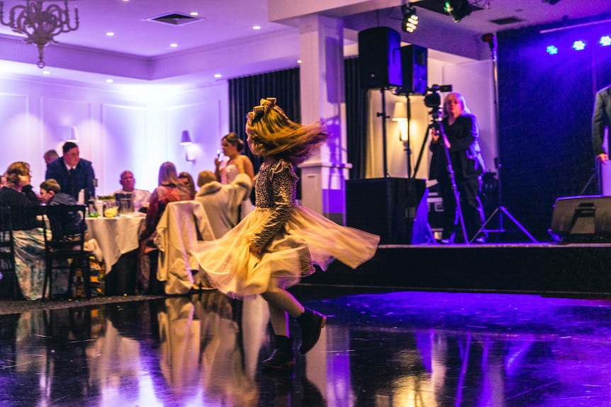 A girl whirls on a dancefloor lit up with bright colours.