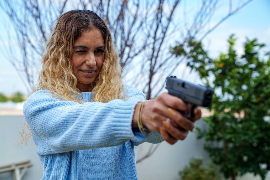A woman aims a handgun.