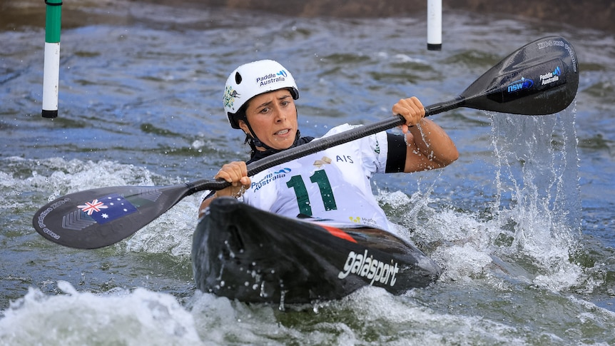 Noemie Fox competing in Canoe Slalom, holding the paddle across her chest, leaning back on the canoe to make it through a gate