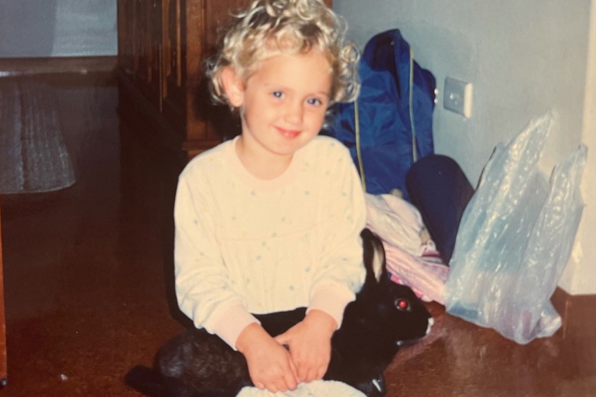 A young girl sitting on the floor holding a black cat.
