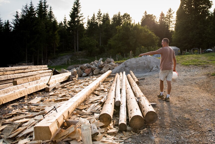 Aljaž walks past a large pile of logs
