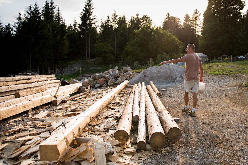 Aljaž walks past a large pile of logs