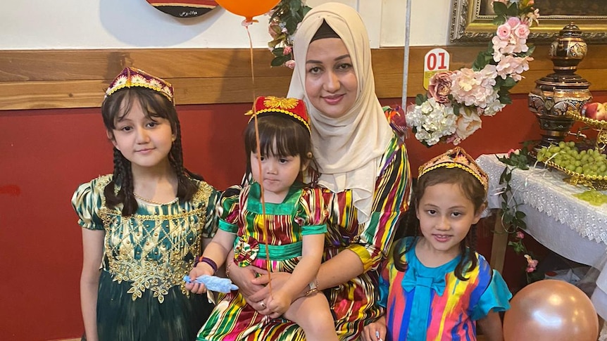 A Uyghur woman sits behind her three children, with balloons in the children's hands. 