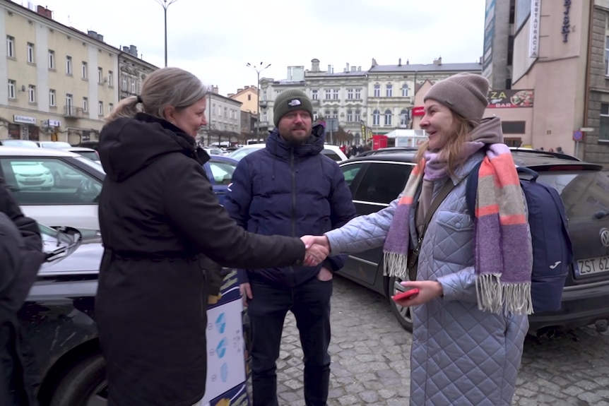 A woman shakes hands with another woman on a street in Poland.