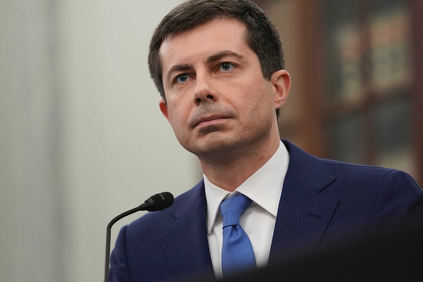 A close up of a man with brown hair and blue eyes wearing a suit and tie