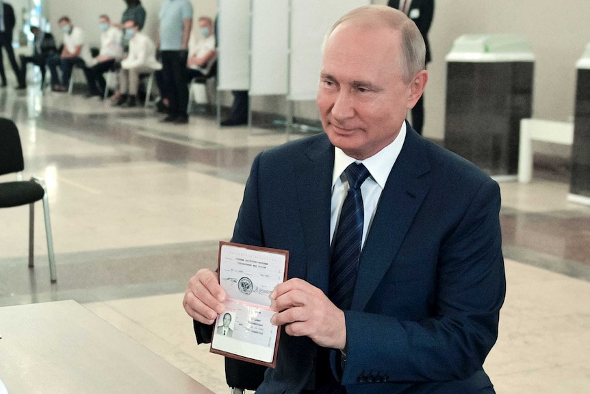 Vladimir Putin, wearing a dark suit and tie shows his passport