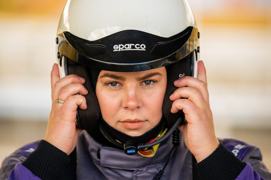 Race car driver Casey Price puts her helmet on her head and looks into the camera.