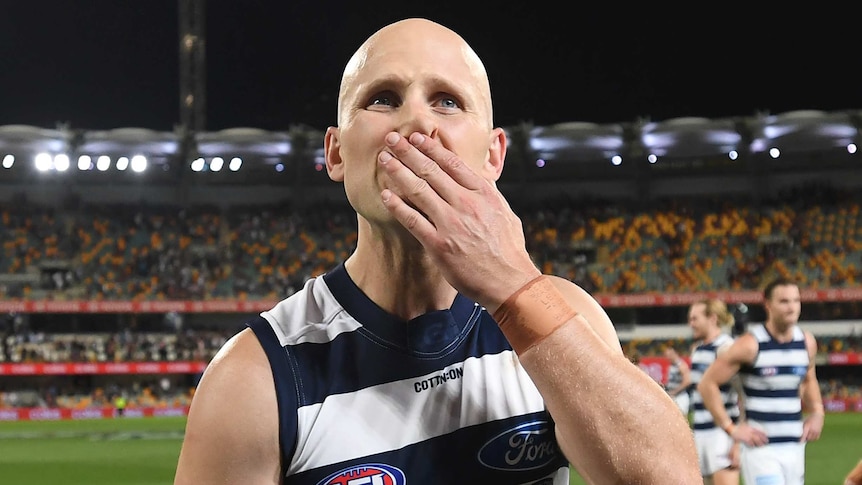 Gary Ablett holds his hand to his mouth and looks up wearing a blue and white striped singlet