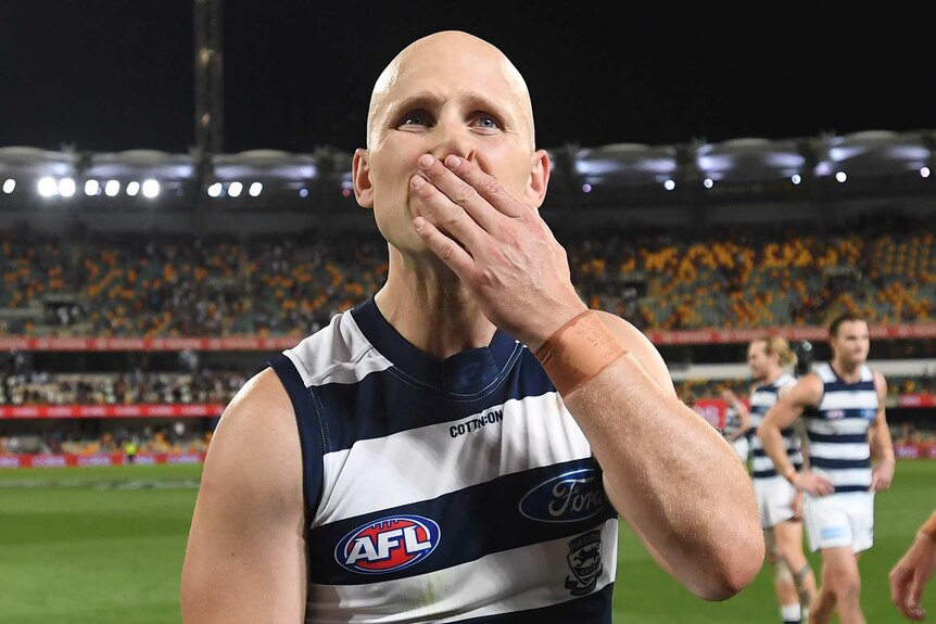 Gary Ablett holds his hand to his mouth and looks up wearing a blue and white striped singlet