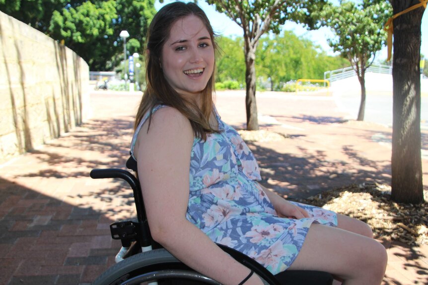 Kaitlyn Jones, in a wheelchair, in front of some trees.
