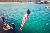 A girl jumps off a jetty into emerald green water at Coffs Harbour.