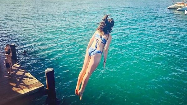 A girl jumps off a jetty into emerald green water at Coffs Harbour.