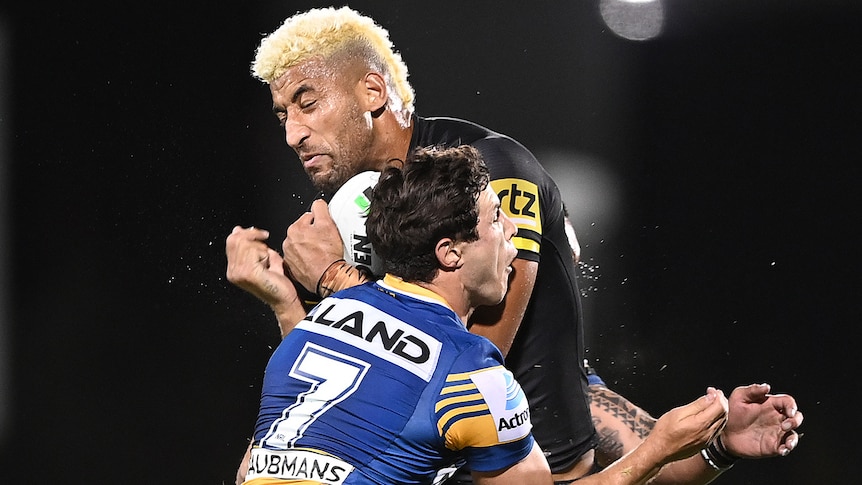 A Penrith Panthers NRL player holds the ball as he is tackled by a Parramatta opponent.