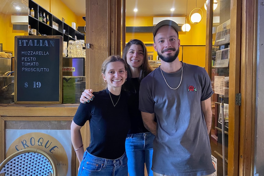 A photo of three people smiling outside of a cafe