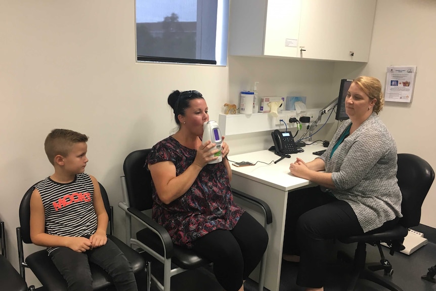 Julie McLeod does an asthma breath test while her six year old son Zen, and clinical research officer Kelly Steel watch