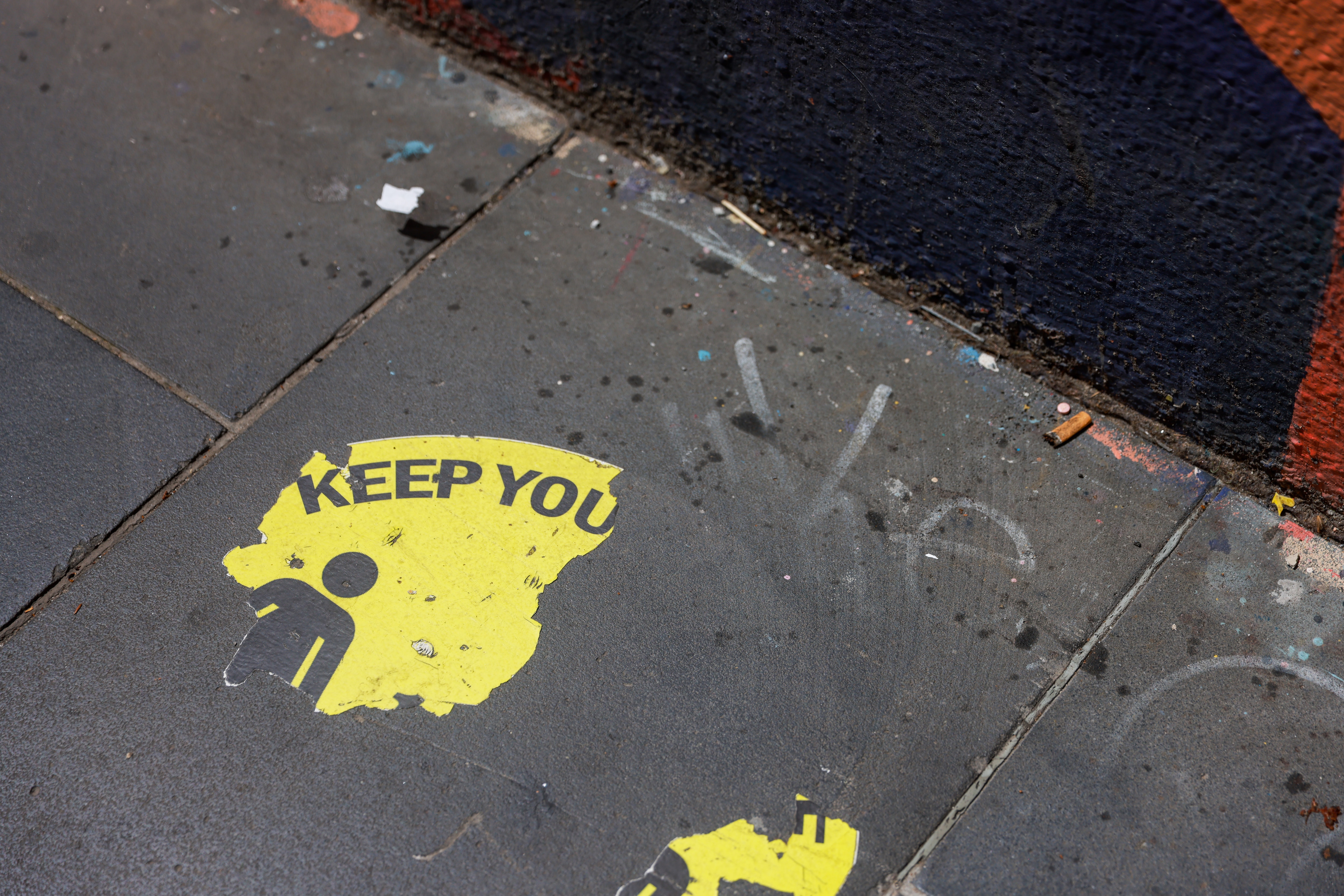 Faded social distance stickers on the footpath and people walking with masks as they pass hand sanitiser stations.