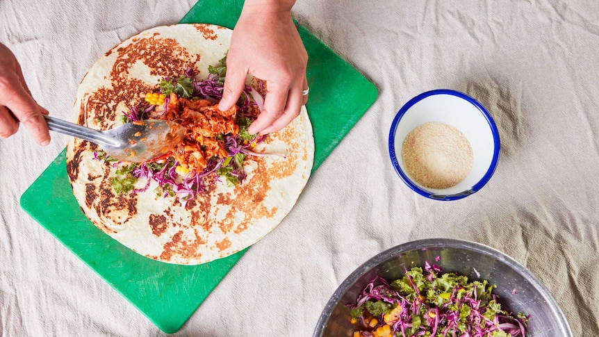A cook spoons the chicken filling into the burrito with a bowl of cabbage, kale and corn slaw alongside, for a family dinner.