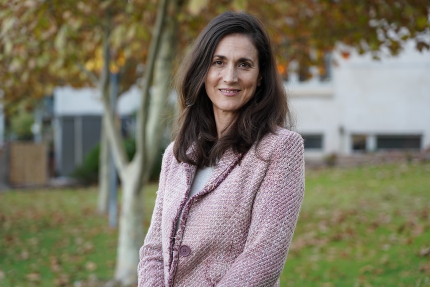 Woman in pink blazer stands outside smiling at camera