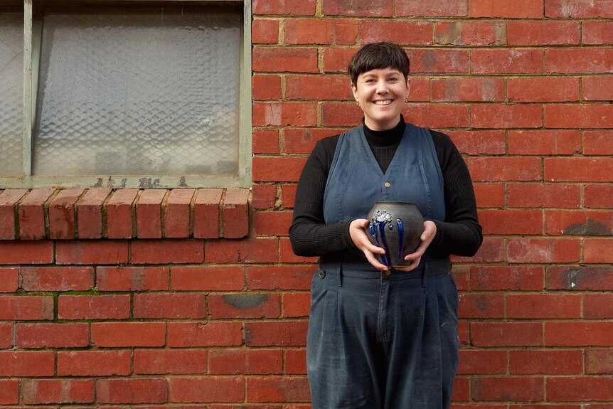 Georgina Proud holds a pot while standing in front of a brick wall.