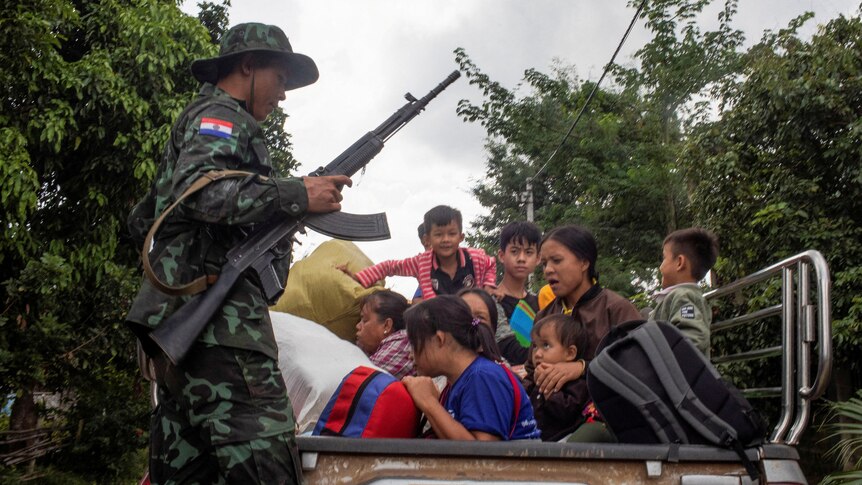 A soldier holding a run looks over a mother and children sitting in the back of a truck