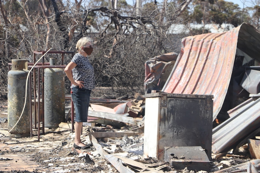 A woman stands looking at a burned down building 